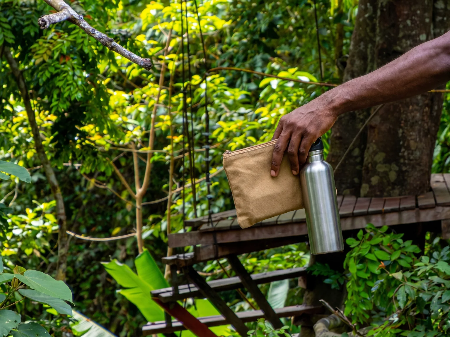 Plain pouch and reusable water bottle carried over wooden decking